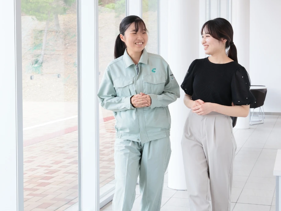 COSMOSの制服を着た女性社員とオフィスカジュアル姿の女性が笑顔で会話している様子