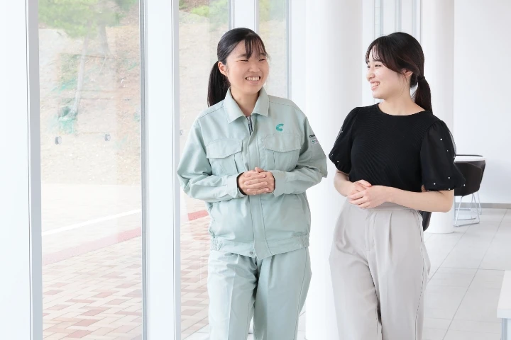 COSMOSの制服を着た女性社員とオフィスカジュアル姿の女性が笑顔で会話している様子